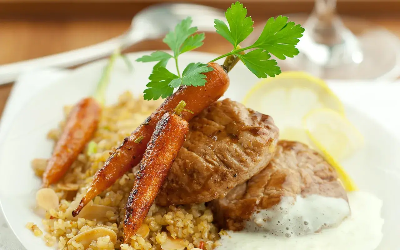 Délicieux grenadin de veau, servi avec des carottes glacées, du boulgour et une sauce crémeuse.