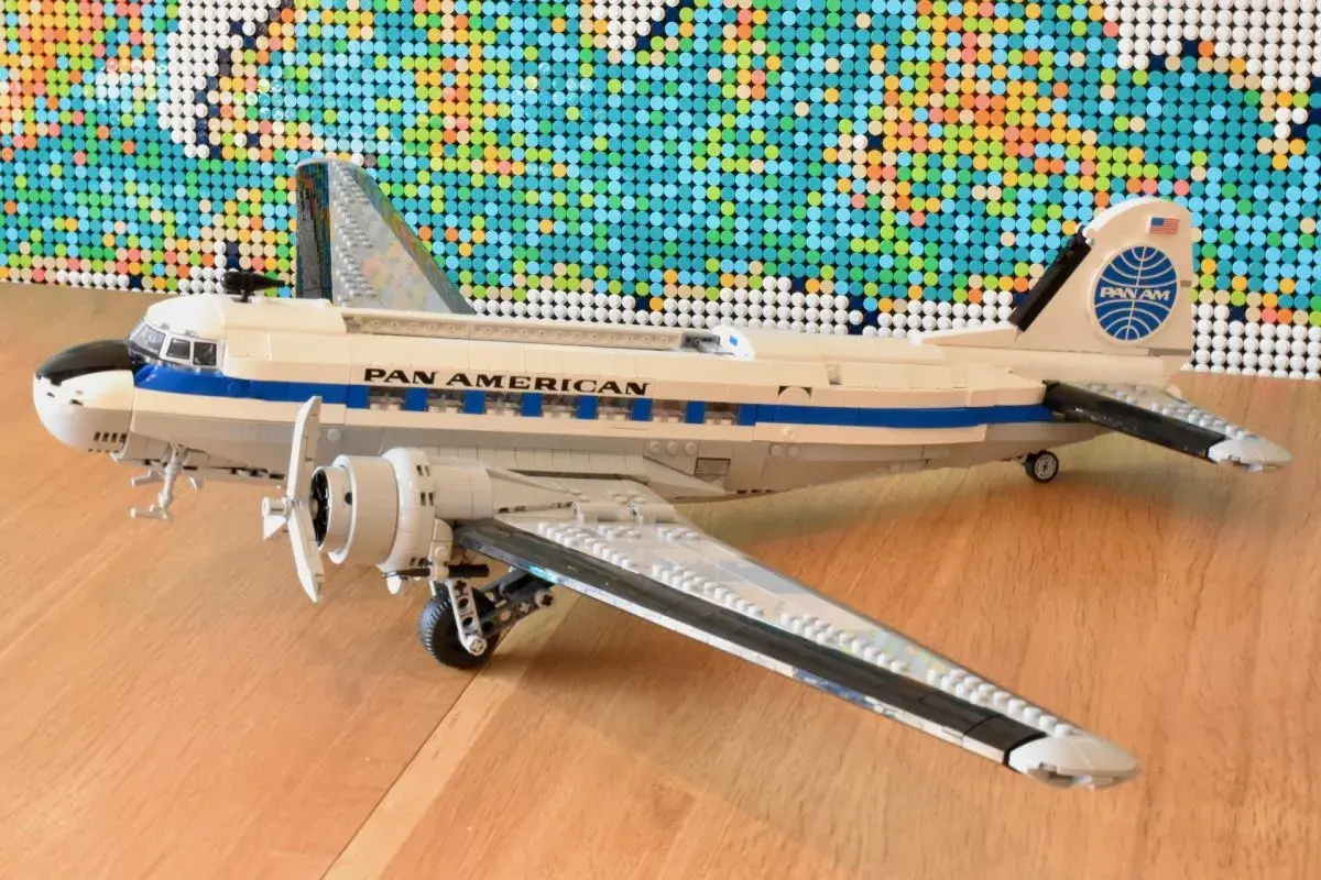 Ein detailreiches Lego DC-3 Flugzeug der Pan Am steht auf einem Holzboden, im Hintergrund eine bunte Lego-Weltkarte.