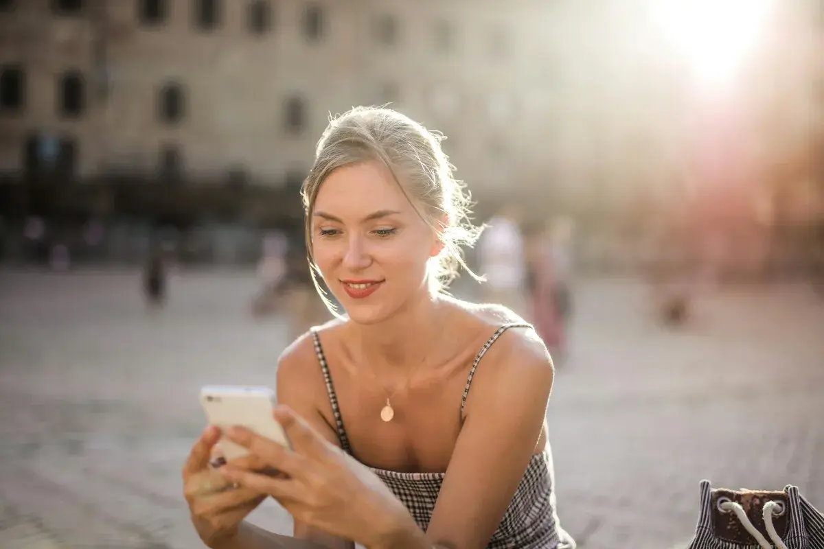 Donna sorride guardando il suo smartphone, forse prenotando un b&b per le vacanze. Luce dorata del tramonto.