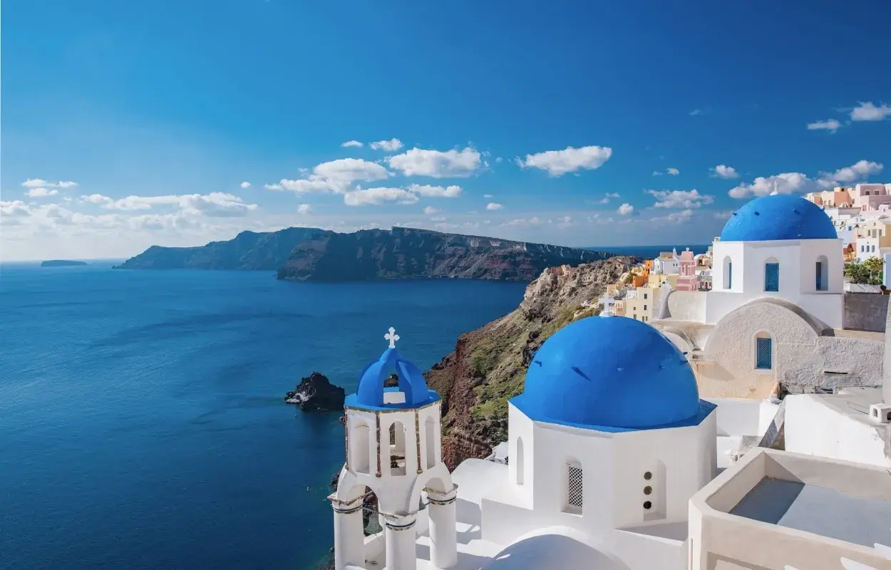 Blaue Kuppeln und weiße Gebäude auf Santorini, ein Traumziel für Griechenland Reisetipps. Die Caldera im Hintergrund.