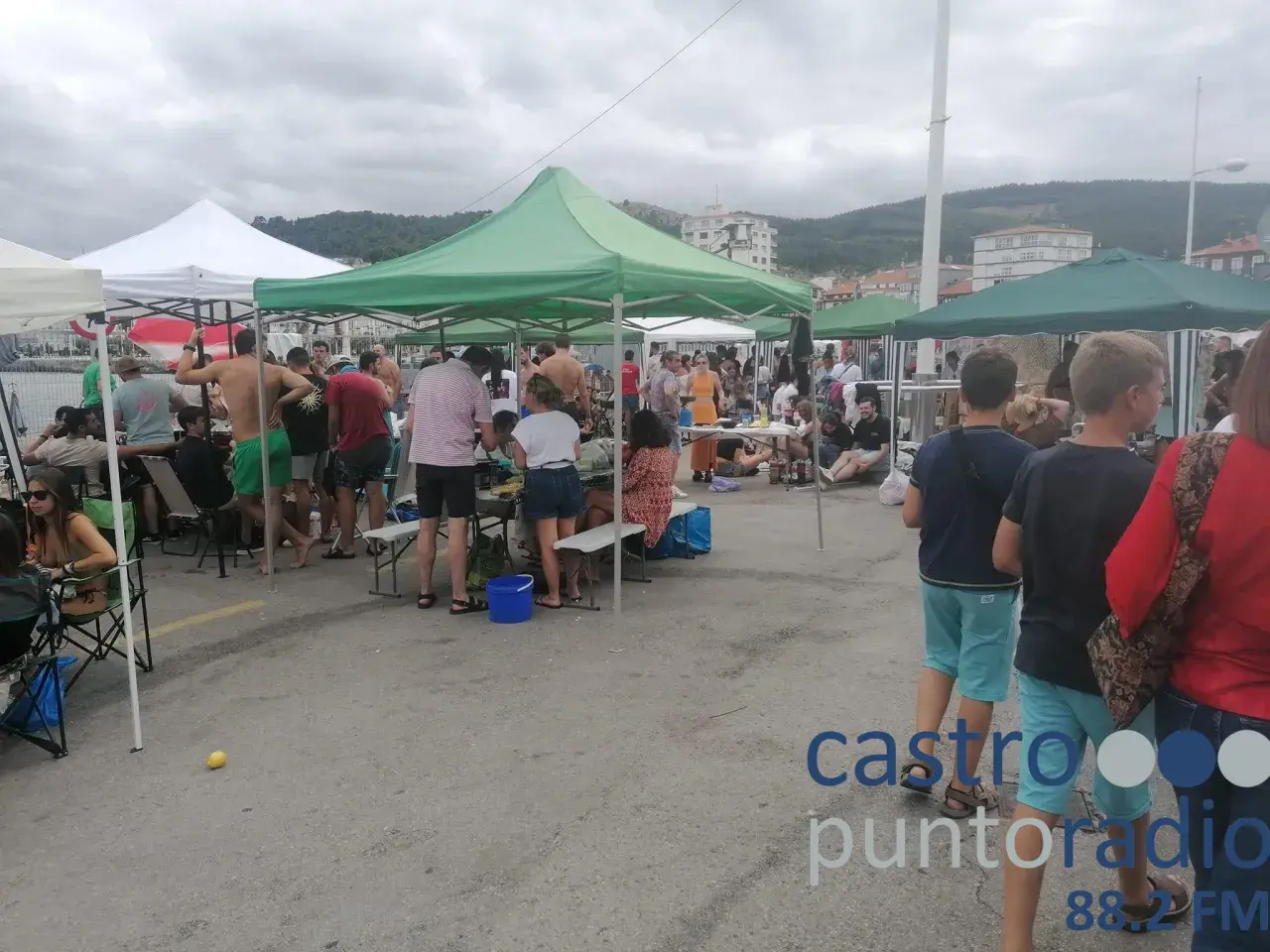 Gente reunida bajo carpas en un evento al aire libre en **Santa Ana, Castro Urdiales**. Un día nublado con ambiente festivo.