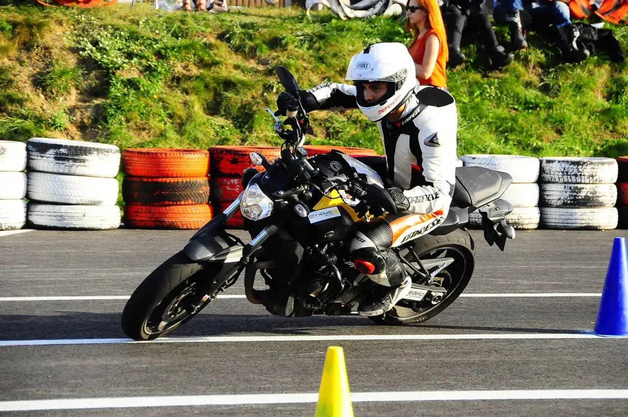 Motocyklista w białym kasku i kombinezonie doskonale opanował pozycję na motocyklu, pochylając się na zakręcie toru.