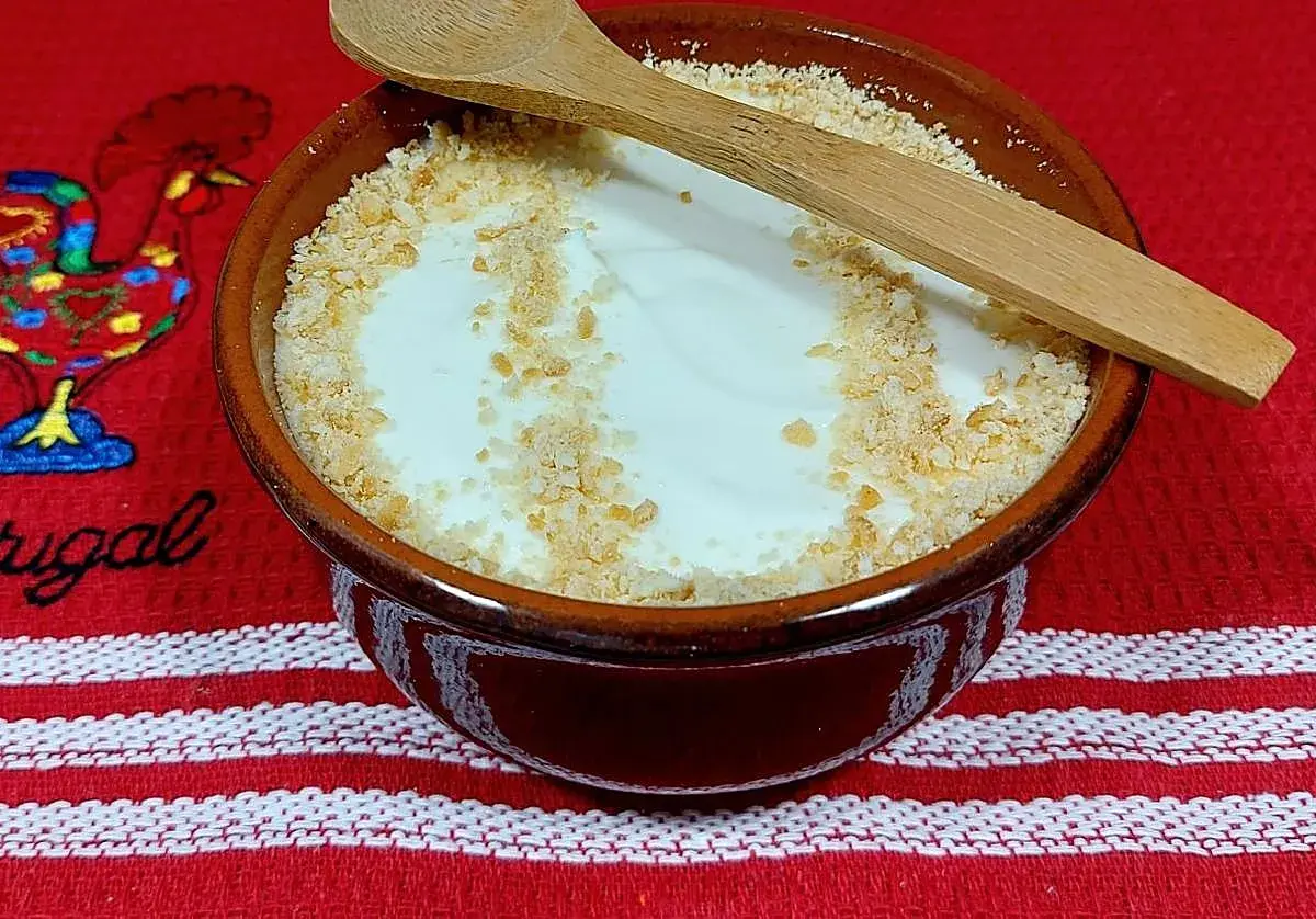 Delicioso serradura portuguesa en cuenco de barro, espolvoreado con galleta triturada y una cuchara de madera.