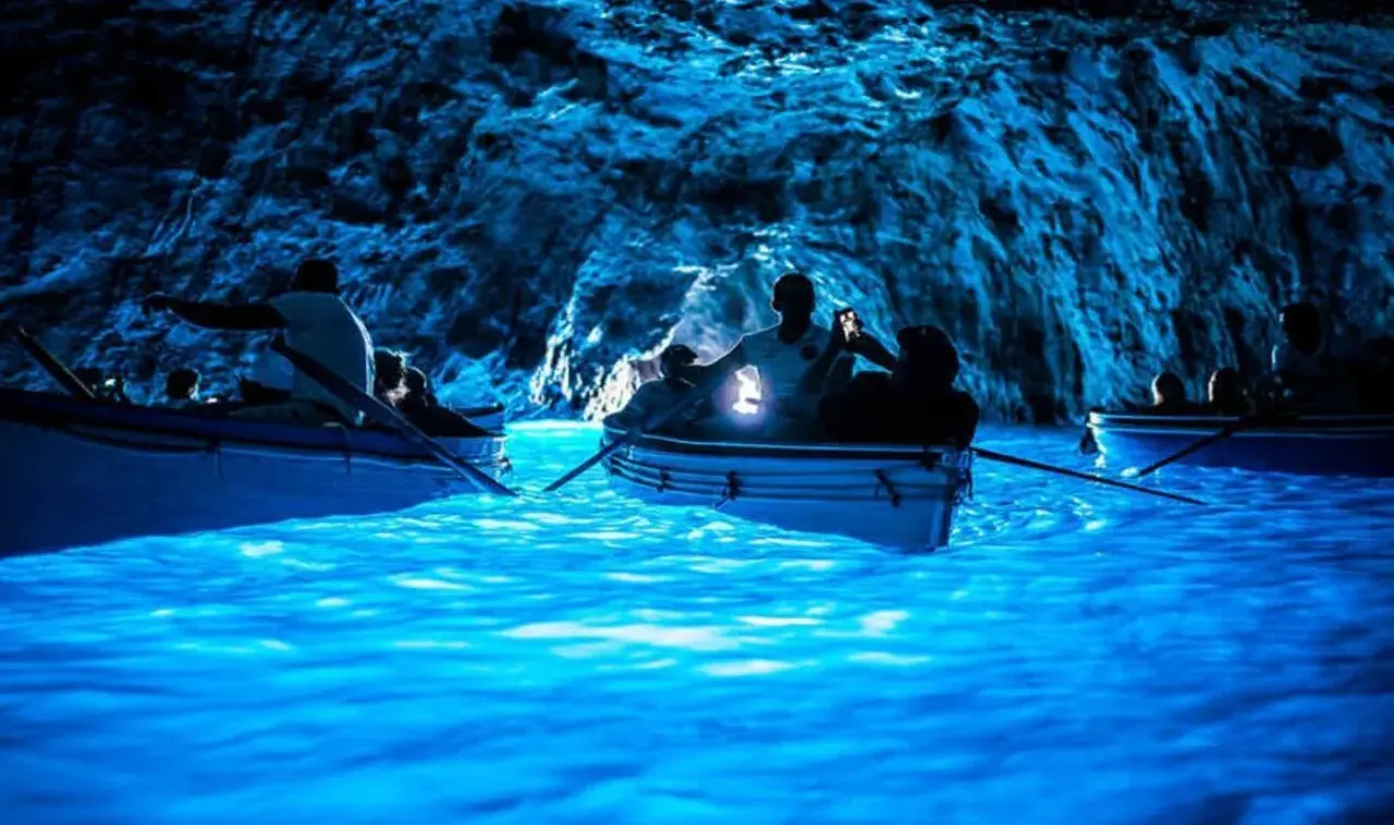 Barche a remi navigano nelle acque luminose della Grotta Azzurra, un luogo magico dove si trova questo spettacolo naturale.