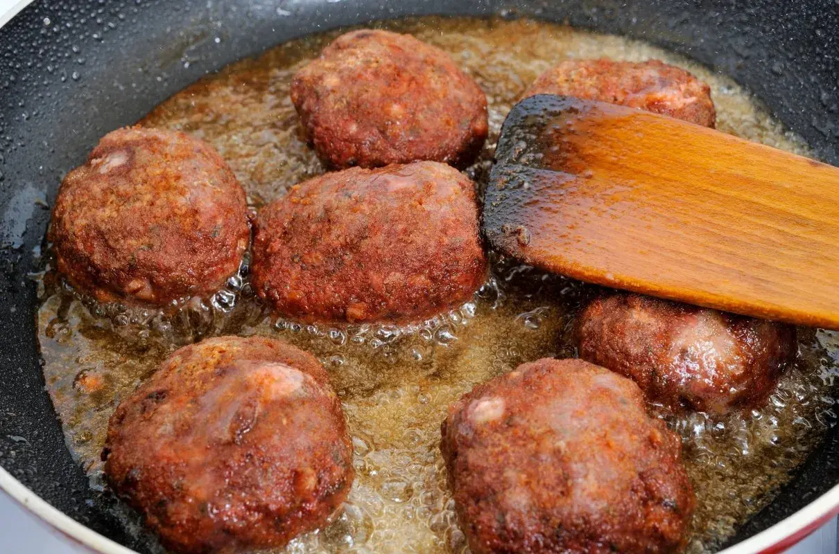 Na patelni smażą się kotlety mielone. Drewniana łopatka pomaga przewracać je, by równomiernie się zarumieniły.