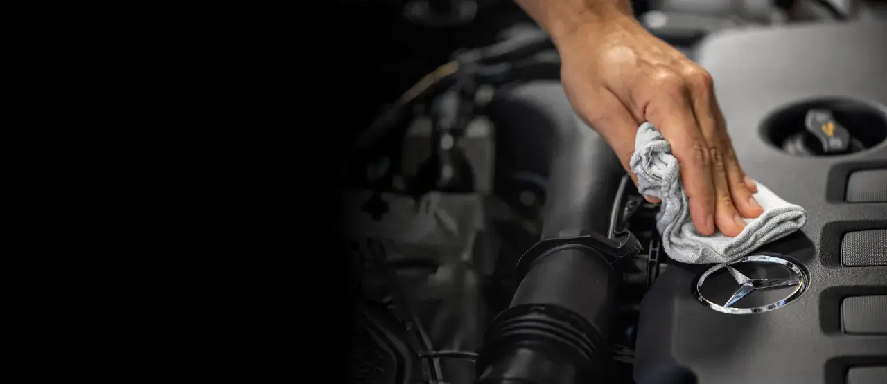 Mano limpiando el logo de Mercedes-Benz. Un detalle para el reset mantenimiento Mercedes.