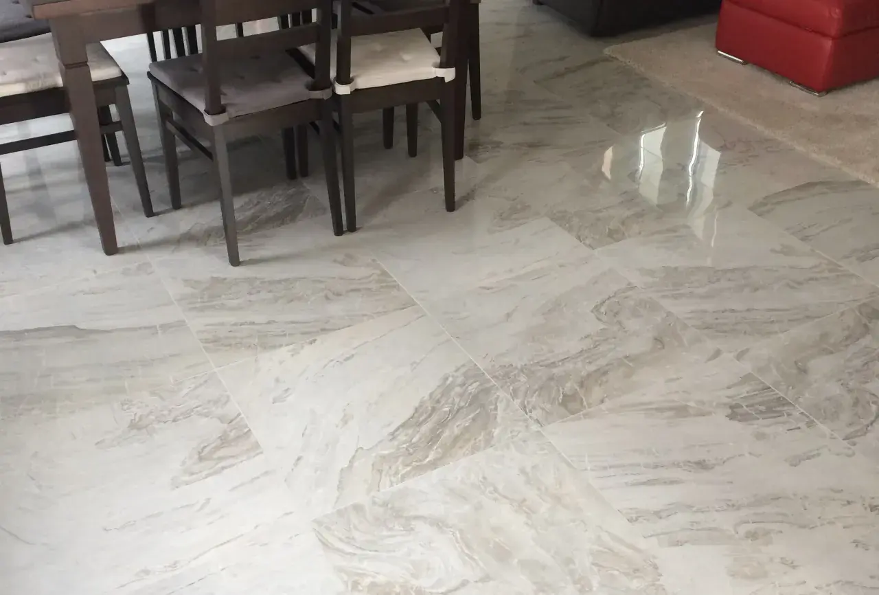 Pavimento in gres porcellanato effetto marmo, con venature grigie e bianche, sotto un tavolo con sedie scure.