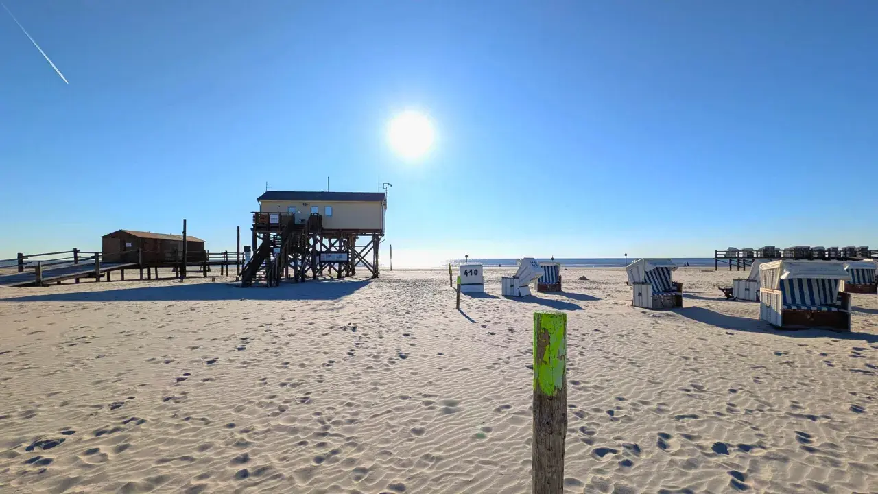Sonniger Tag am St. Peter-Ording Strand mit Strandkörben und Stelzenhäusern.