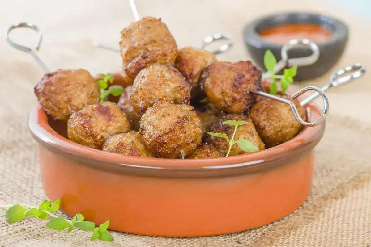Polpette di tacchino dorate e succulente, cotte nella friggitrice ad aria, servite in una ciotola di terracotta con erbe aromatiche.
