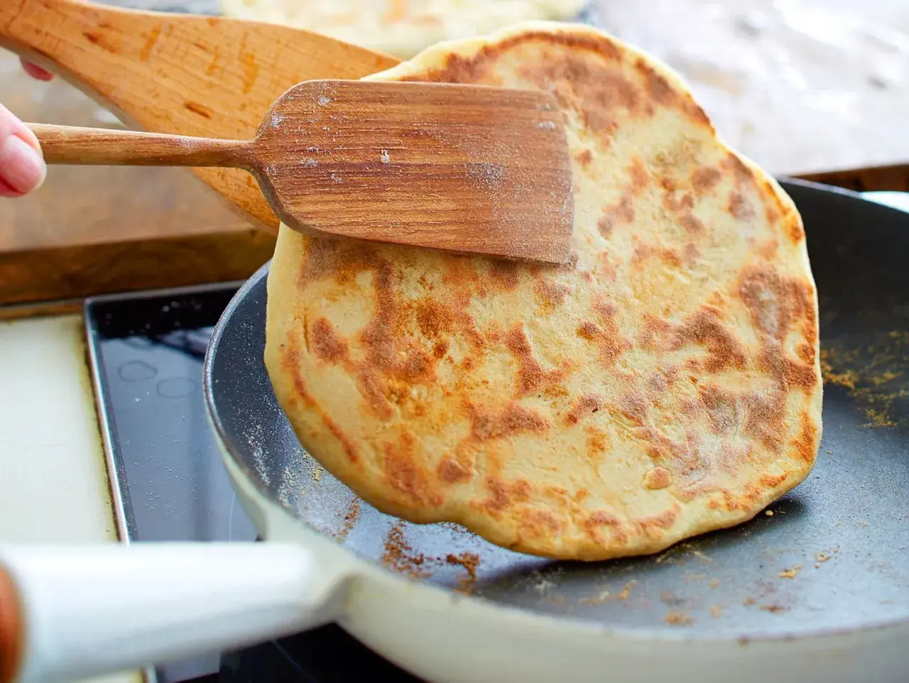 Ein goldbraunes Pfannenbrot wird mit einem Holzspatel in einer Pfanne gewendet. Perfekt für ein einfaches Pfannenbrot Rezept.