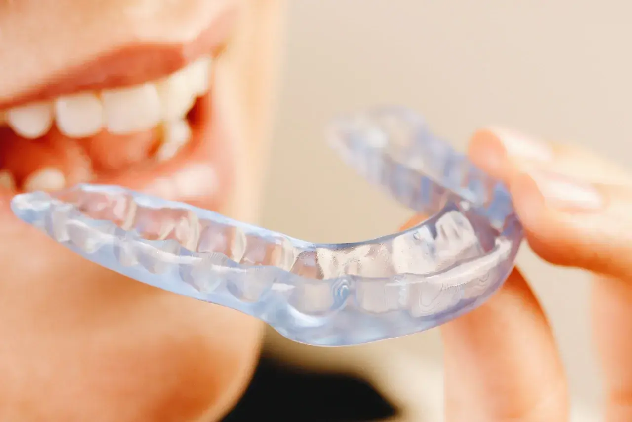 Persona sonriente sostiene una férula Invisalign transparente, lista para mejorar su sonrisa.