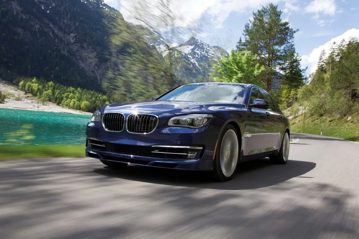 Granatowy BMW Alpina B7 mknie po górskiej drodze, obok turkusowego jeziora i ośnieżonych szczytów.