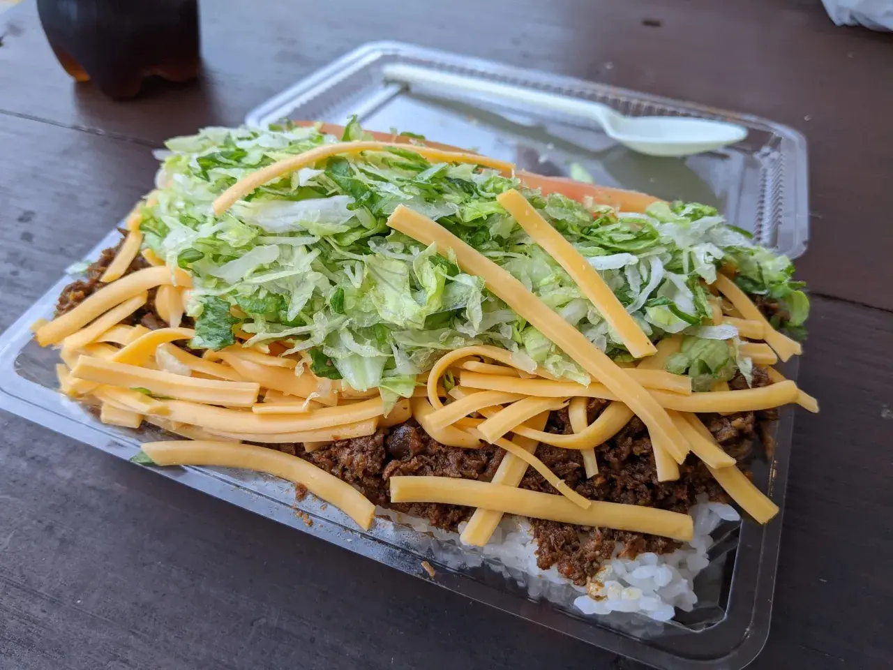 A hearty Okinawa taco rice dish, layered with white rice, seasoned ground meat, shredded lettuce, and melted cheese, ready to be enjoyed.