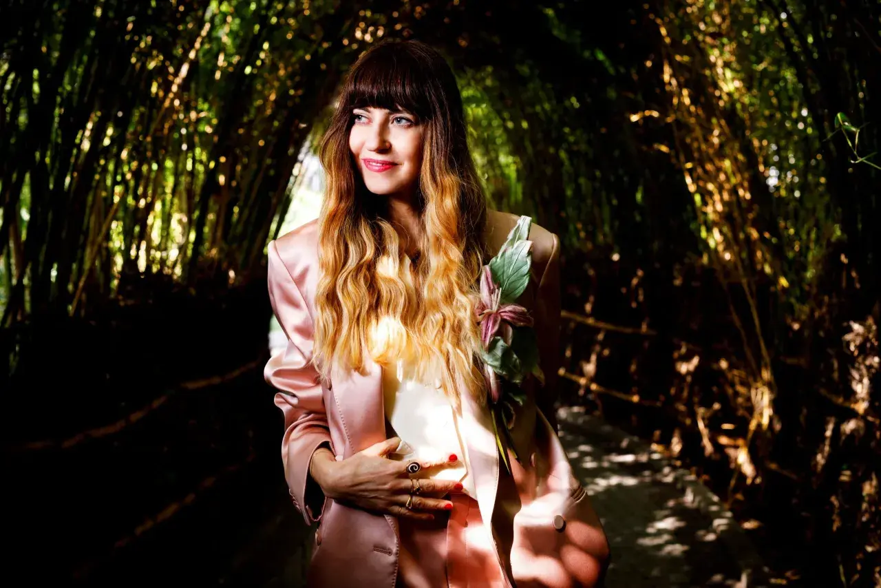 Chiara Tagliaferri, con un tailleur rosa e un fiore sul petto, posa in un tunnel di bambù illuminato dal sole.