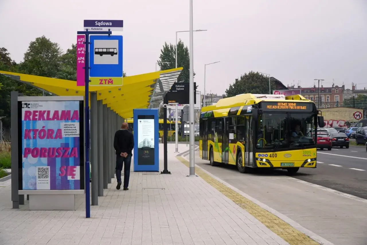 Dworzec autobusowy Katowice Sądowa. Żółty autobus elektryczny zatrzymuje się na przystanku. Rozkład jazdy widoczny na tablicy informacyjnej.