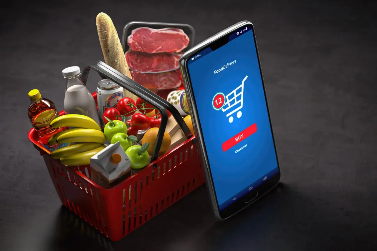 Koszyk z zakupami i smartfon z aplikacją do zamawiania jedzenia. M-commerce ułatwia zakupy spożywcze.