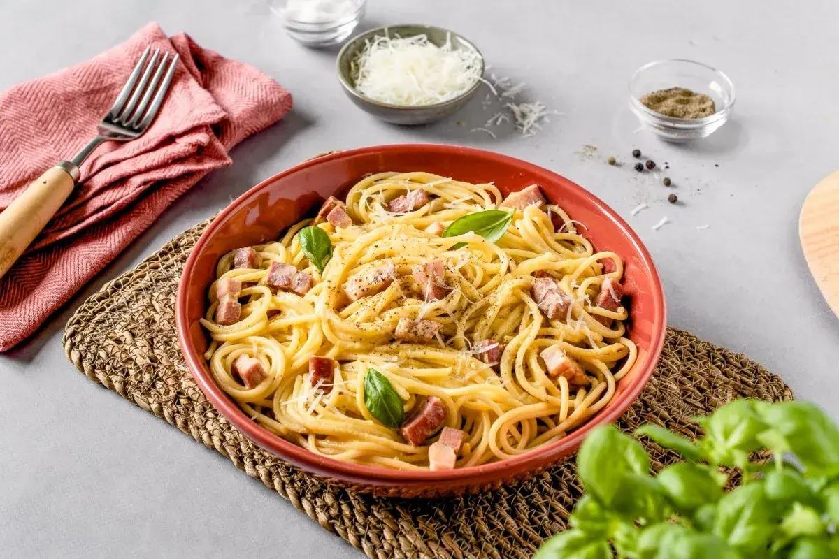 Un plato de carbonara italia, con espagueti, trozos de panceta, queso rallado y hojas de albahaca fresca.