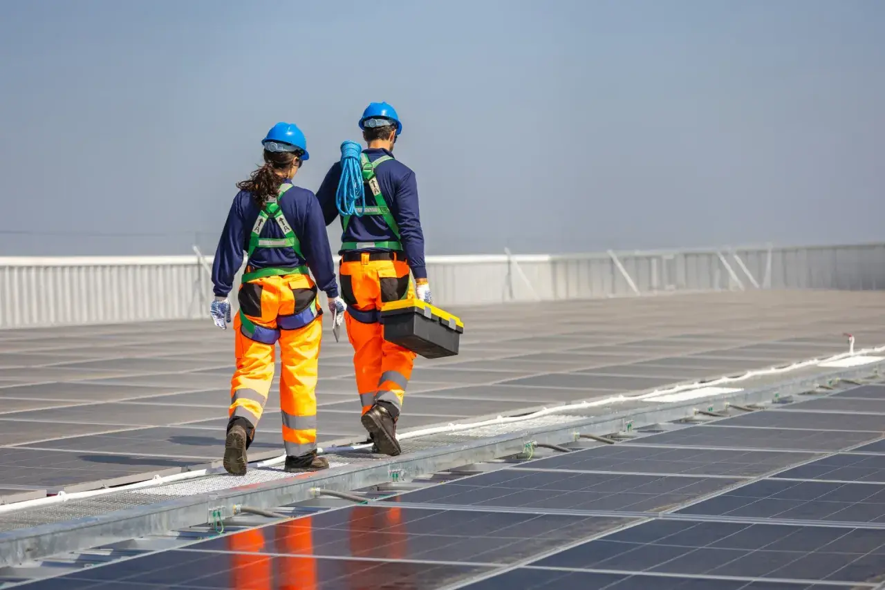 Zwei Techniker in Schutzkleidung gehen über eine Photovoltaikanlage. Regelmäßige Wartung der Photovoltaikanlage ist Pflicht für optimale Leistung.