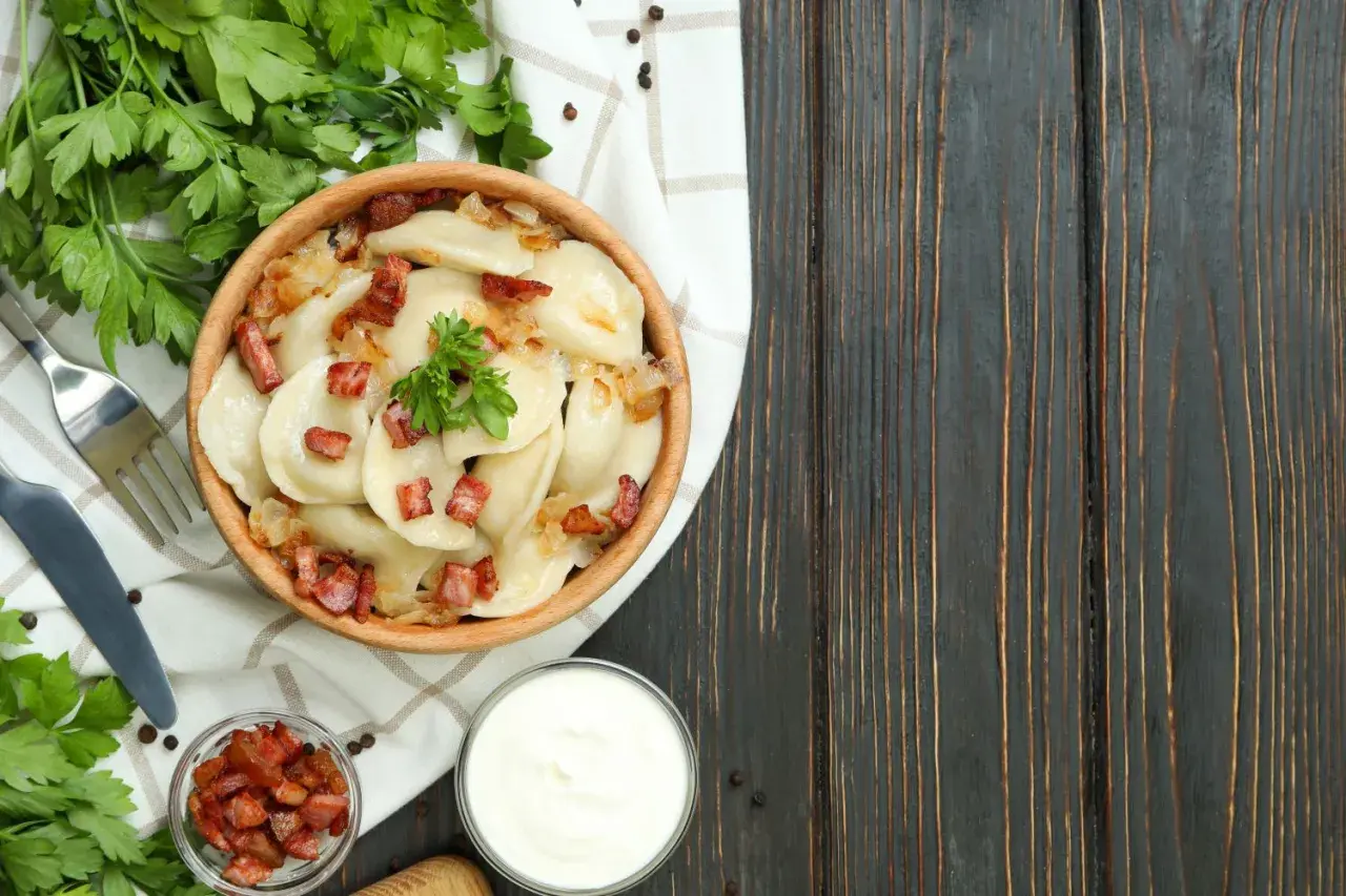 Pyszne pierogi z cebulką i skwarkami, serwowane w drewnianej misce. To klasyka kuchni łemkowskiej, podana z kwaśną śmietaną i świeżą natką pietruszki.