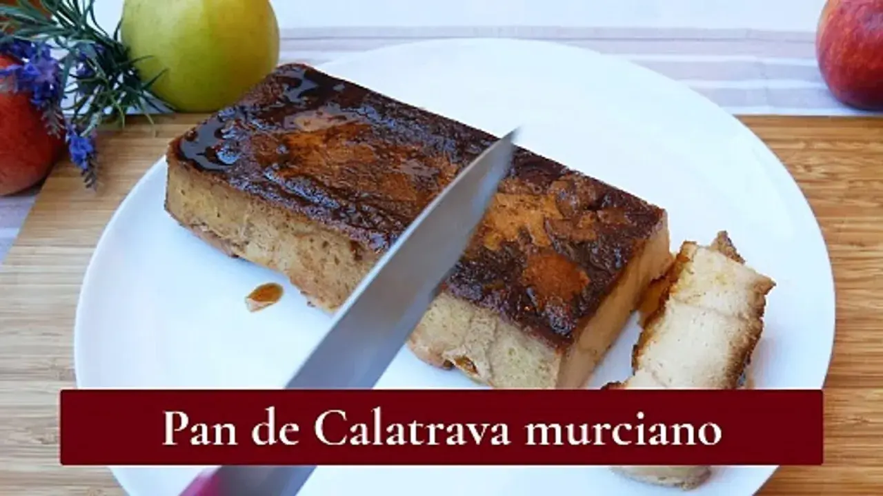 Un cuchillo corta un trozo de pan de Calatrava murciano, un postre dulce y dorado, servido en un plato blanco.