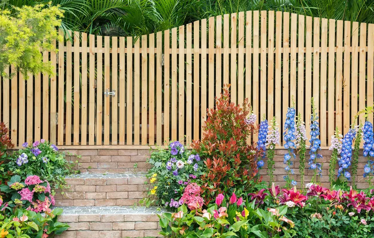 Holz-Gartenzaun-Ideen: Ein schmaler Holzzaun mit Tor, flankiert von bunten Blumen und Ziegelstufen, schafft einen charmanten Eingang.