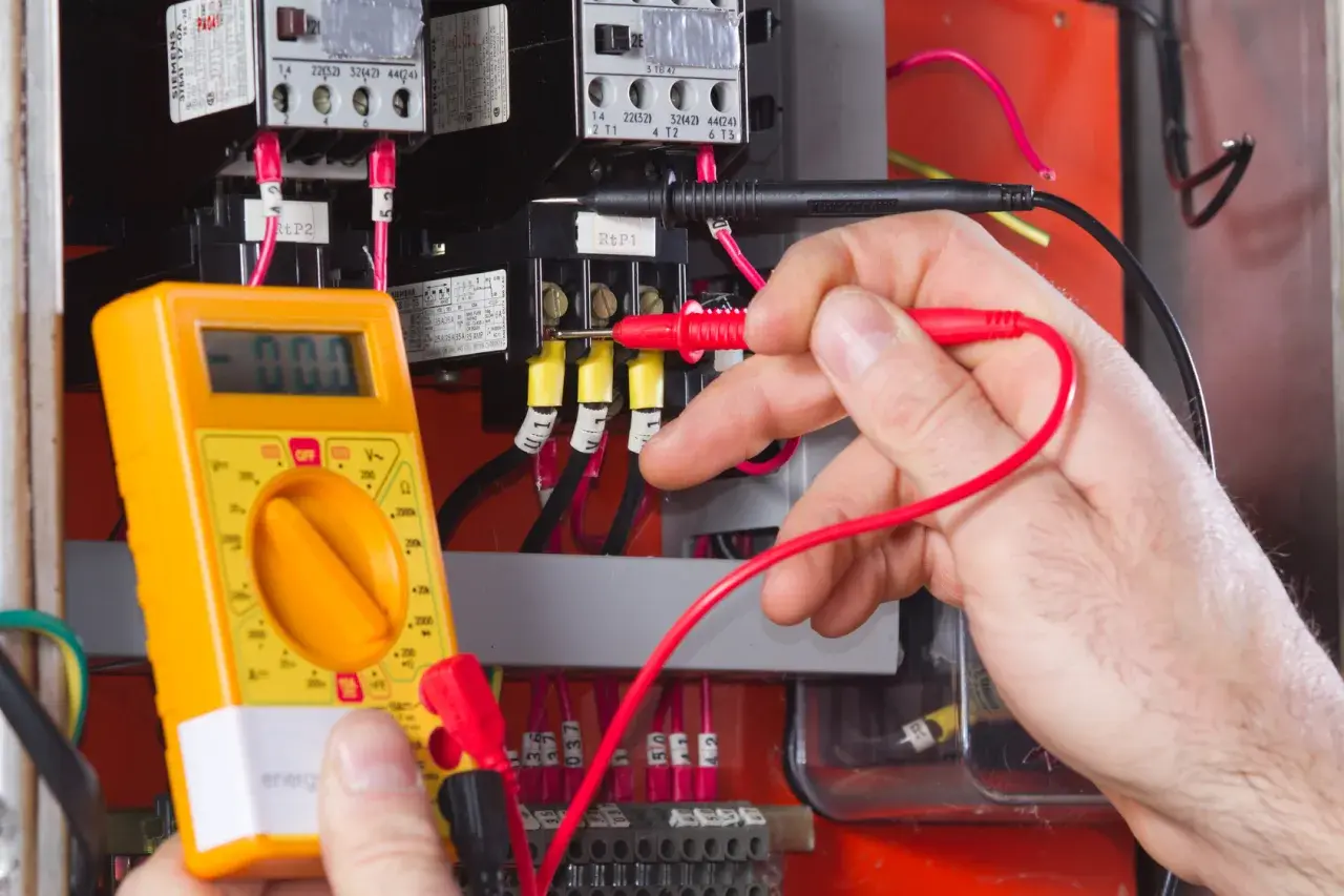Elektromonter z multimetrem sprawdza instalację elektryczną. To praca wymagająca precyzji, zgodna z zawodem elektromonter kod 311101.