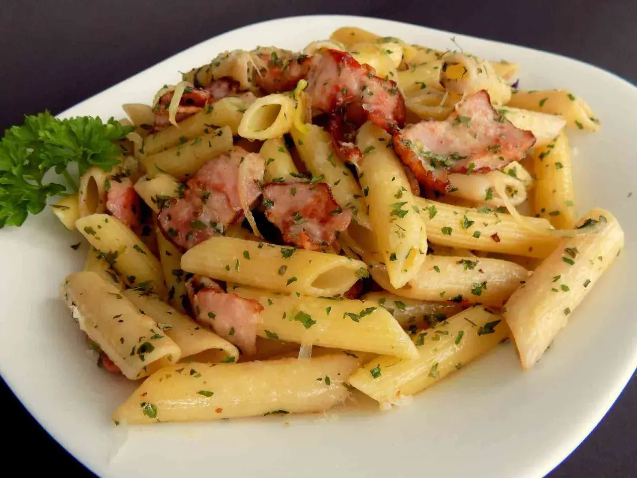 Pyszny makaron penne z kawałkami wędzonego boczku i posypany natką pietruszki. Idealny makaron na obiad.