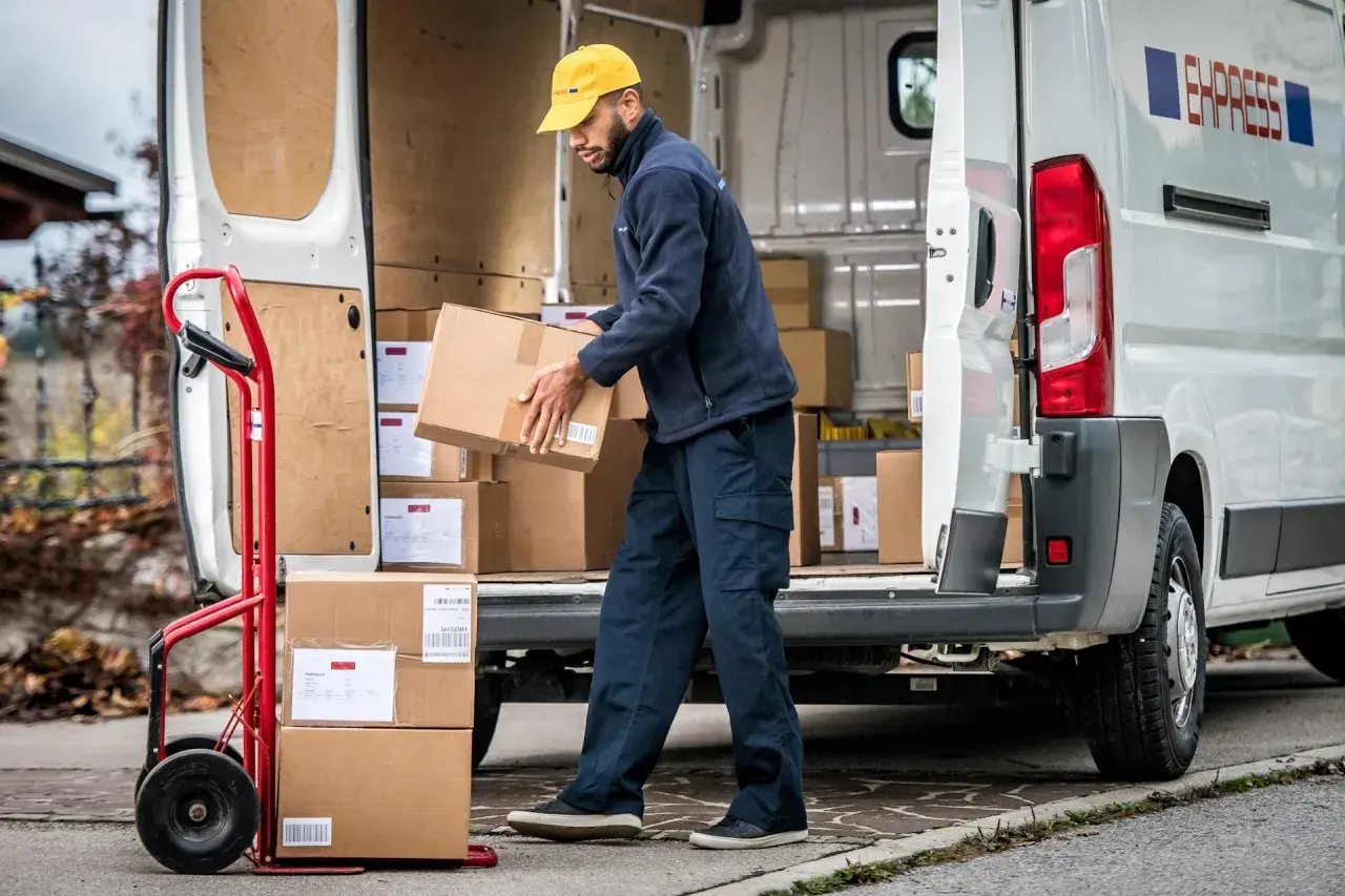 Zusteller lädt Pakete aus einem Lieferwagen. Viele Pakete, vielleicht wegen des peak season surcharge.