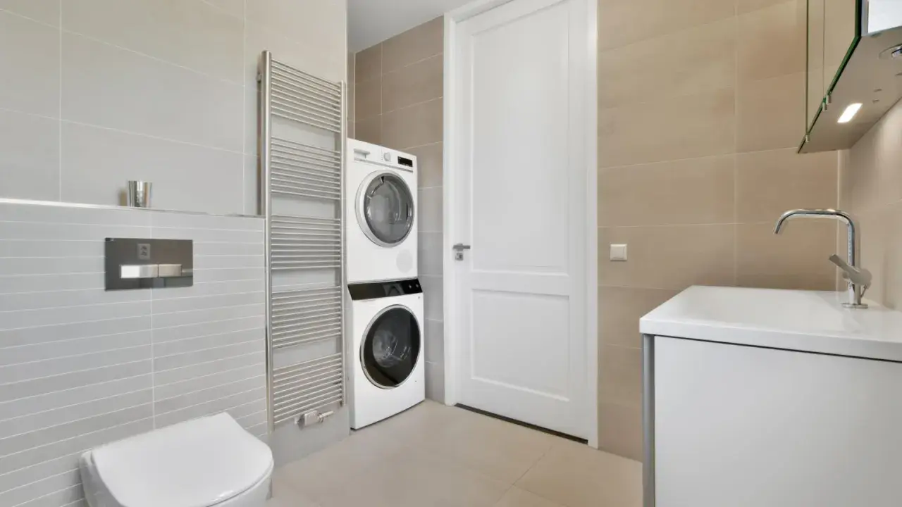 Bagno moderno con doccia e lavatrice vicine. Asciugatrice sopra la lavatrice, vicino a un termosifone cromato e un WC.