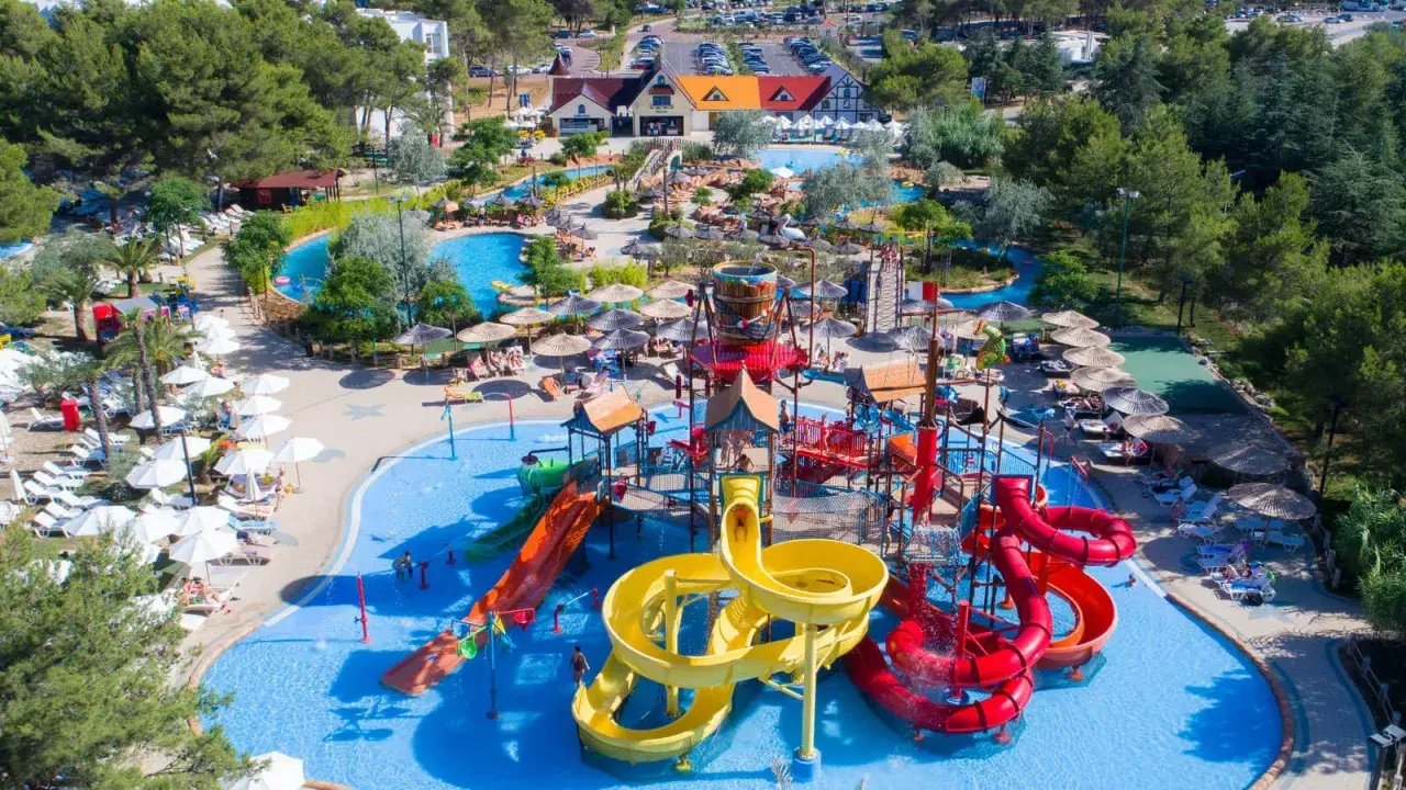 Un camping pour camping-car avec parc aquatique, offrant toboggans colorés, piscines et parasols pour des vacances en famille sous le soleil.
