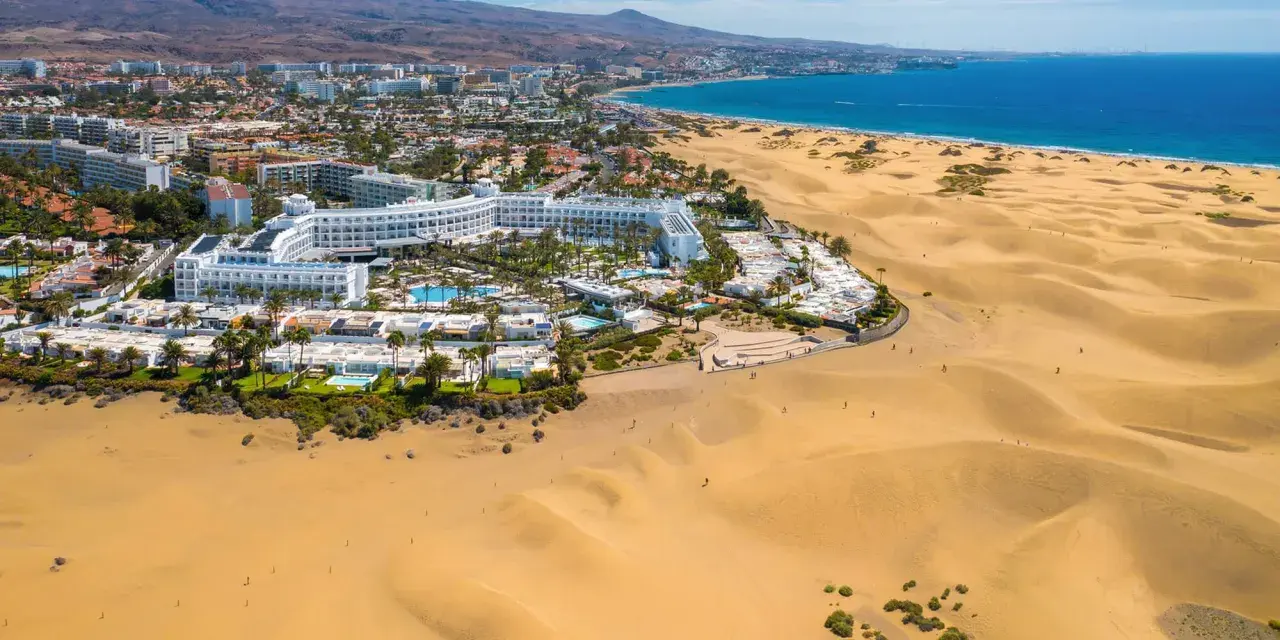 Das Riu Palace Maspalomas thront majestätisch am Rande der goldenen Dünen, mit dem blauen Meer im Hintergrund.