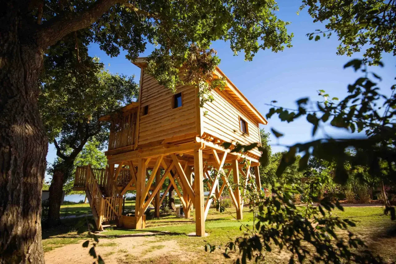 Une **cabane dans les arbres** en bois, perchée sur pilotis, invite à l'aventure dans un cadre verdoyant du **Pays de la Loire**.