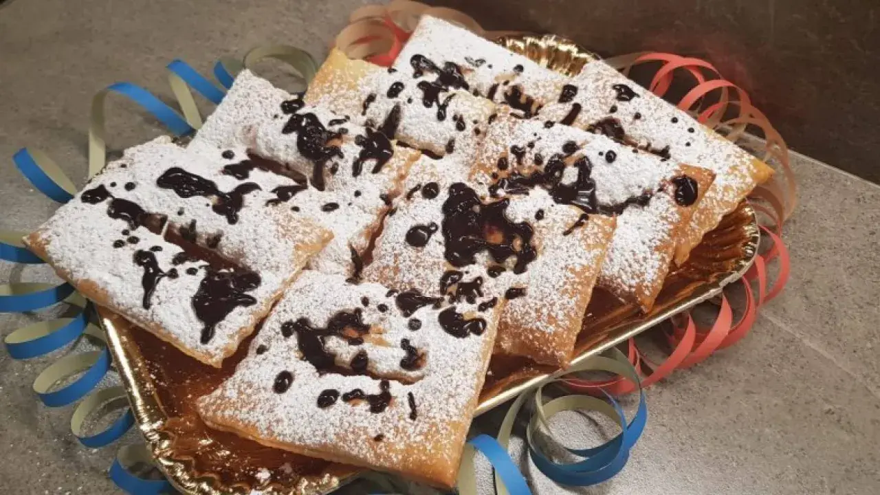 Chiacchiere morbide cosparse di zucchero a velo e gocce di cioccolato, pronte per festeggiare il Carnevale.