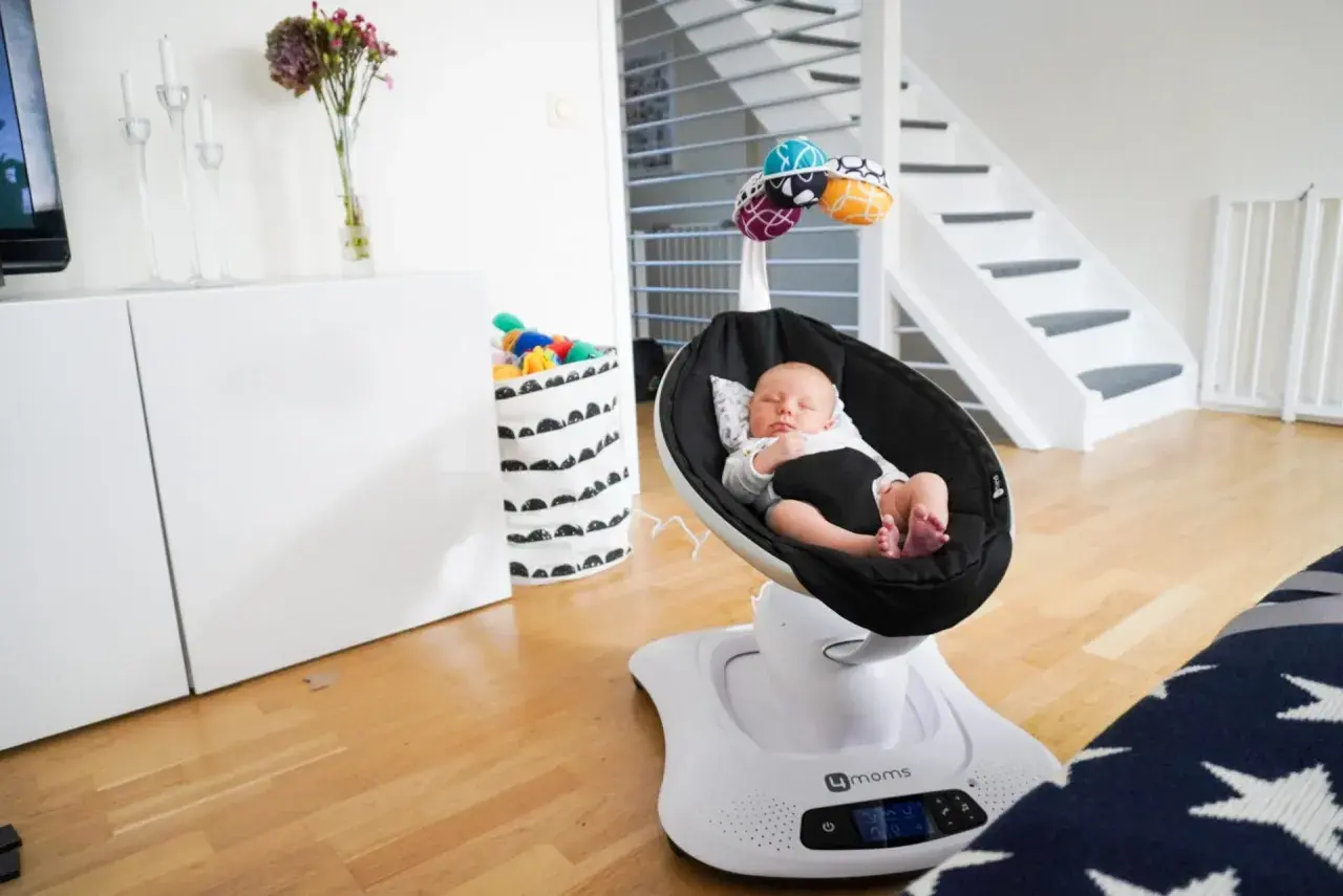 Sover gott i sin mamaroo babysitter. En bebis vilar i en svart gunga med leksaker ovanför.
