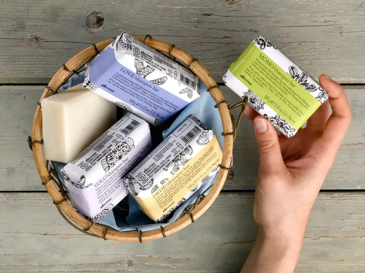 Scopri come si usa lo shampoo solido Davines: una mano sceglie una saponetta profumata da un cesto.