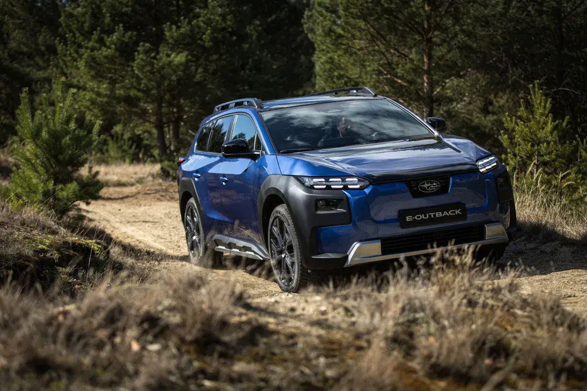 Niebieskie Subaru E-Outback pokonuje piaszczystą drogę wśród drzew. Jazda Subaru po bezdrożach.