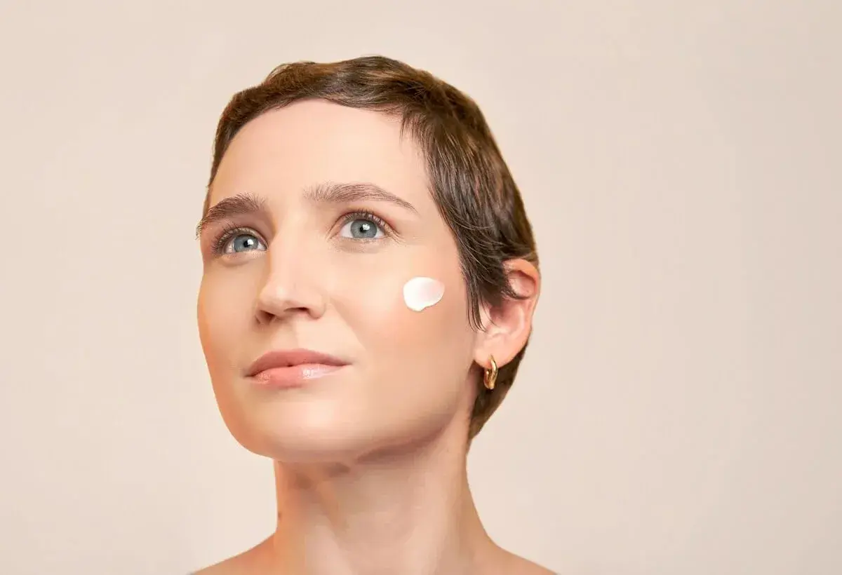 Une femme au regard pensif, avec une touche de crème solaire avant ou après crème hydratante sur la joue.