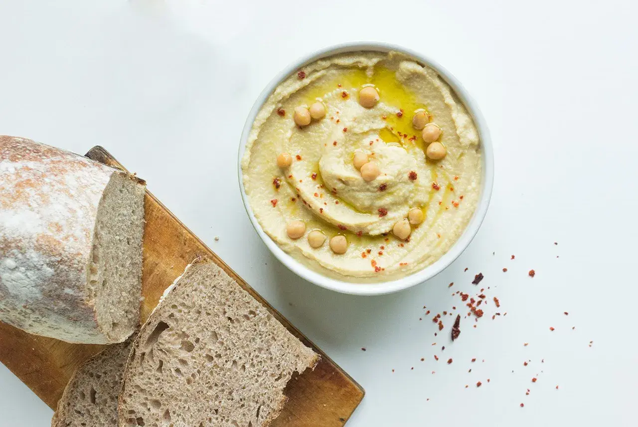 Misternie ułożony hummus z ciecierzycą i oliwą, obok chleba. Czy hummus ma dużo białka? Tak, to świetne źródło!