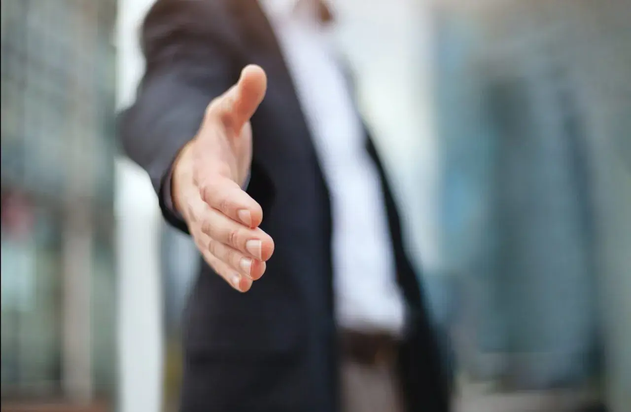 Biznesmen wyciąga rękę do uścisku, symbolizując partnerstwo i współpracę. Dowiedz się, jak założyć spółkę cywilną.