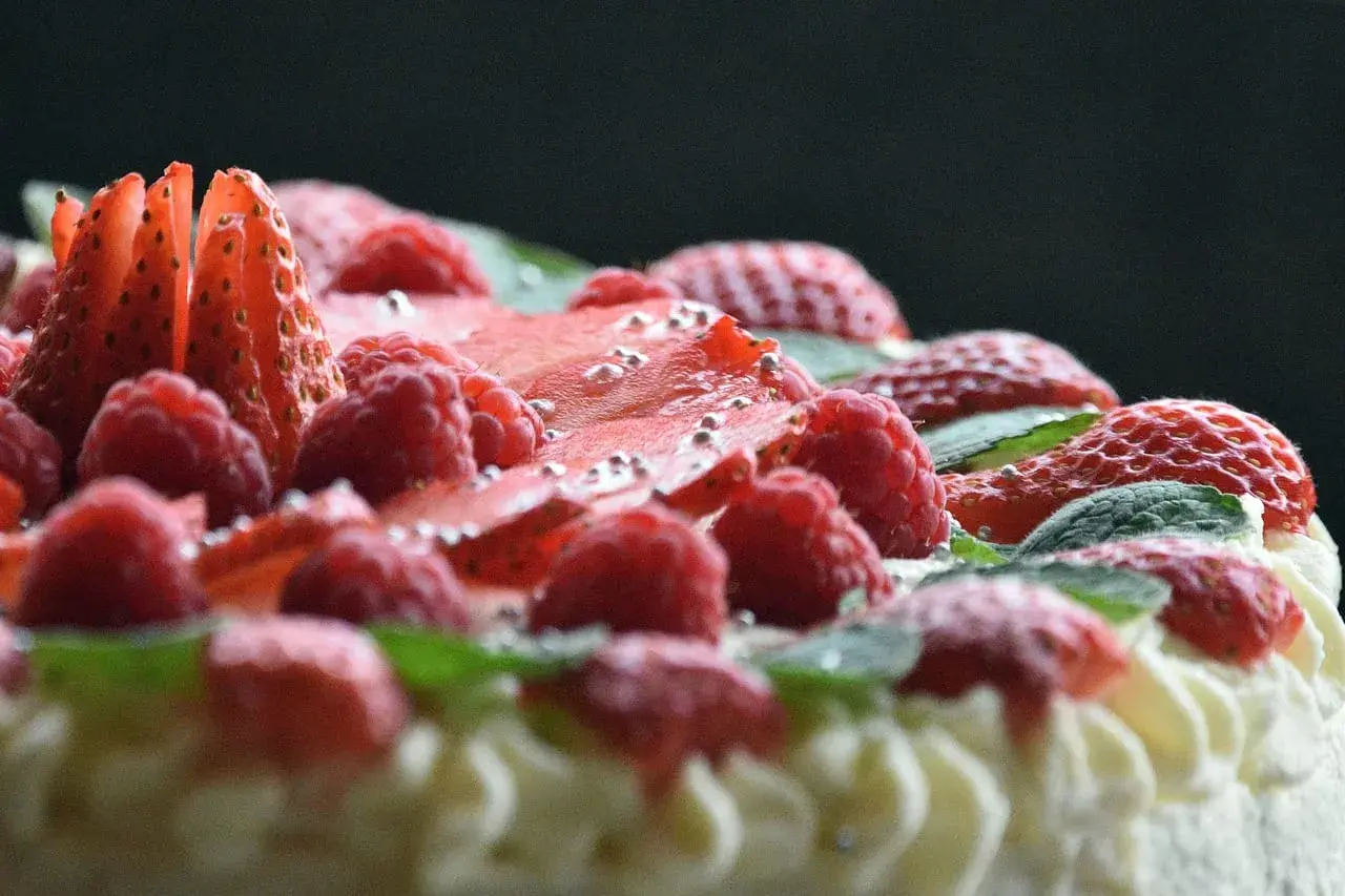Pyszny tort dobosza, udekorowany malinami, truskawkami i listkami mięty, posypany srebrnymi kuleczkami.
