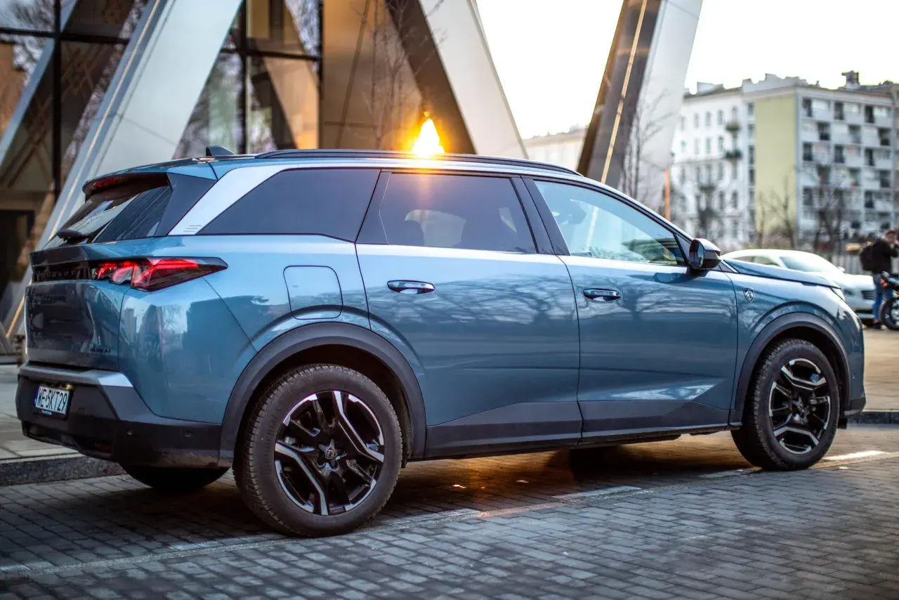 Niebieski Peugeot 5008 na tle nowoczesnej architektury. Wiele osób szuka peugeot 5008 opinie przed zakupem.