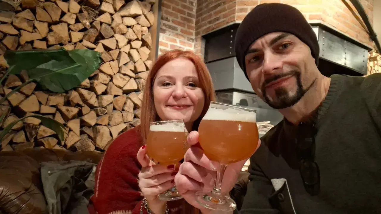 Coppia brinda con birra artigianale alla huisbrouwerij de halve maan. Sfondo rustico con legna e mattoni.