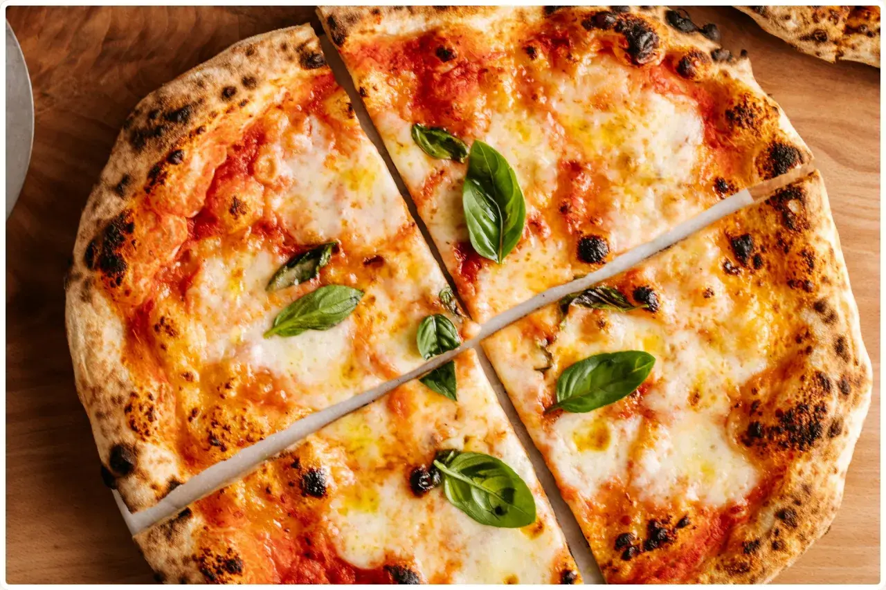 Margherita z puszystym ciastem i prawdziwym sosem do pizzy, ozdobiona świeżą bazylią.