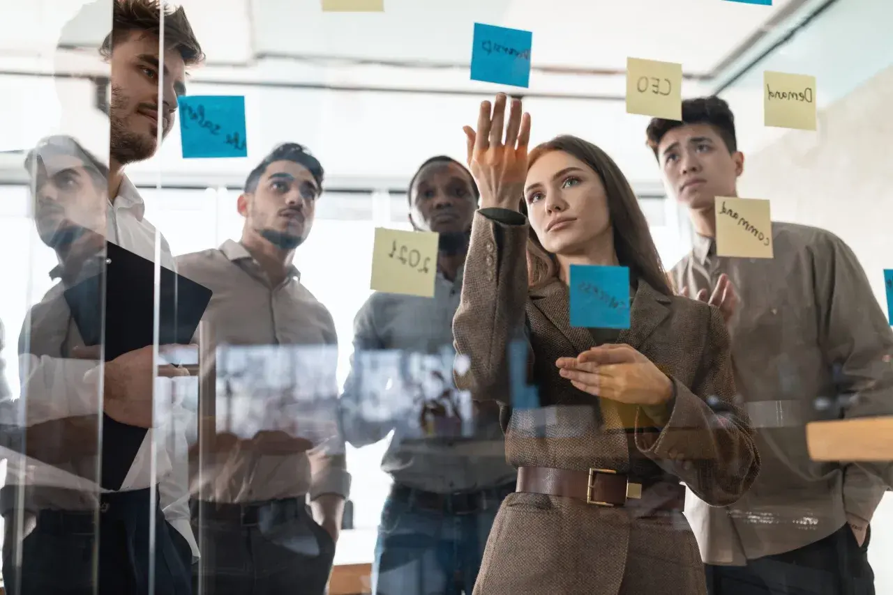 Team discute idee su lavagna di vetro, con post-it che indicano obiettivi e strategie per il **premio produzione**.