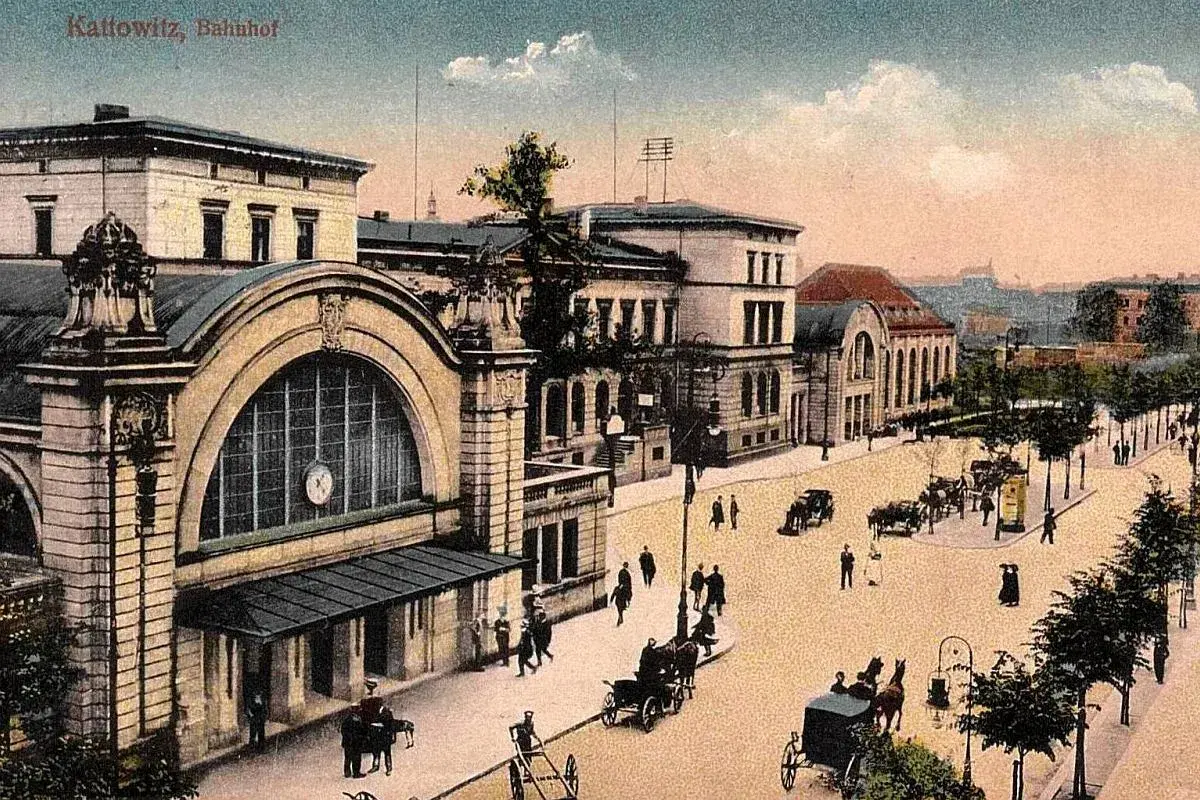 Dawny dworzec w Katowicach z epoki, z dorożkami i pieszymi na brukowanym placu.
