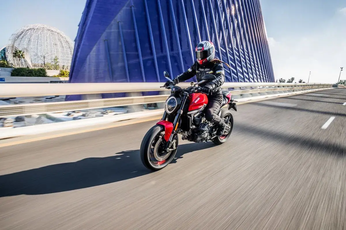Mujer conduce moto roja por puente moderno. Con 18 años, puedes sacarte el carnet de moto A2.