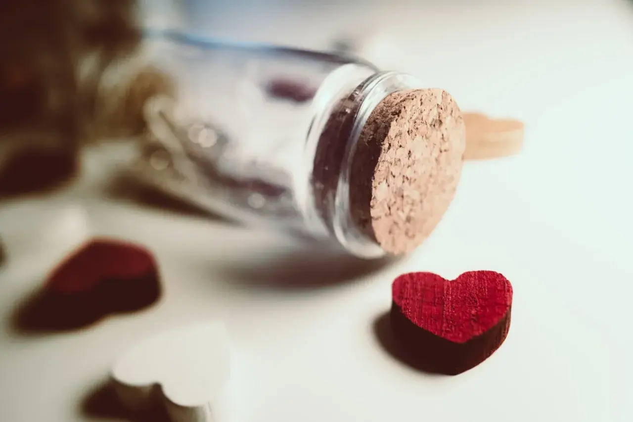 Cuore rosso vicino a una bottiglia tappata, simbolo di innamoramento e amore.