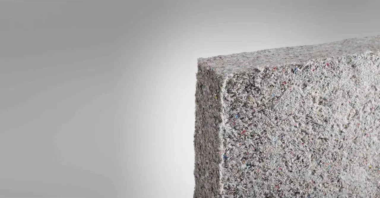 Bloque de material aislante grisáceo, similar a fibra de vidrio triturada. Evitar respirar estas partículas para prevenir consecuencias.
