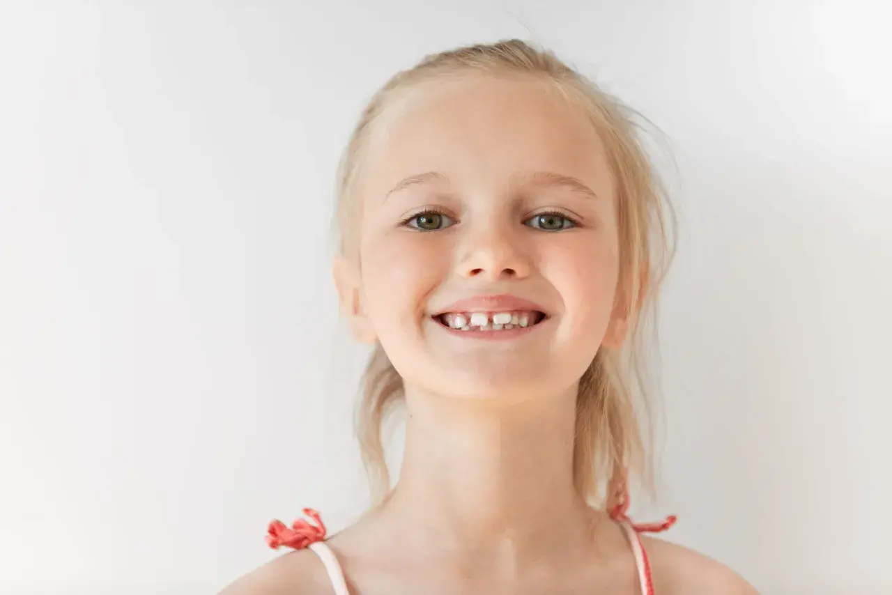 Uśmiechnięta dziewczynka z blond włosami, kiedy rosna 6 ząbków, pokazuje swoje nowe mleczaki.