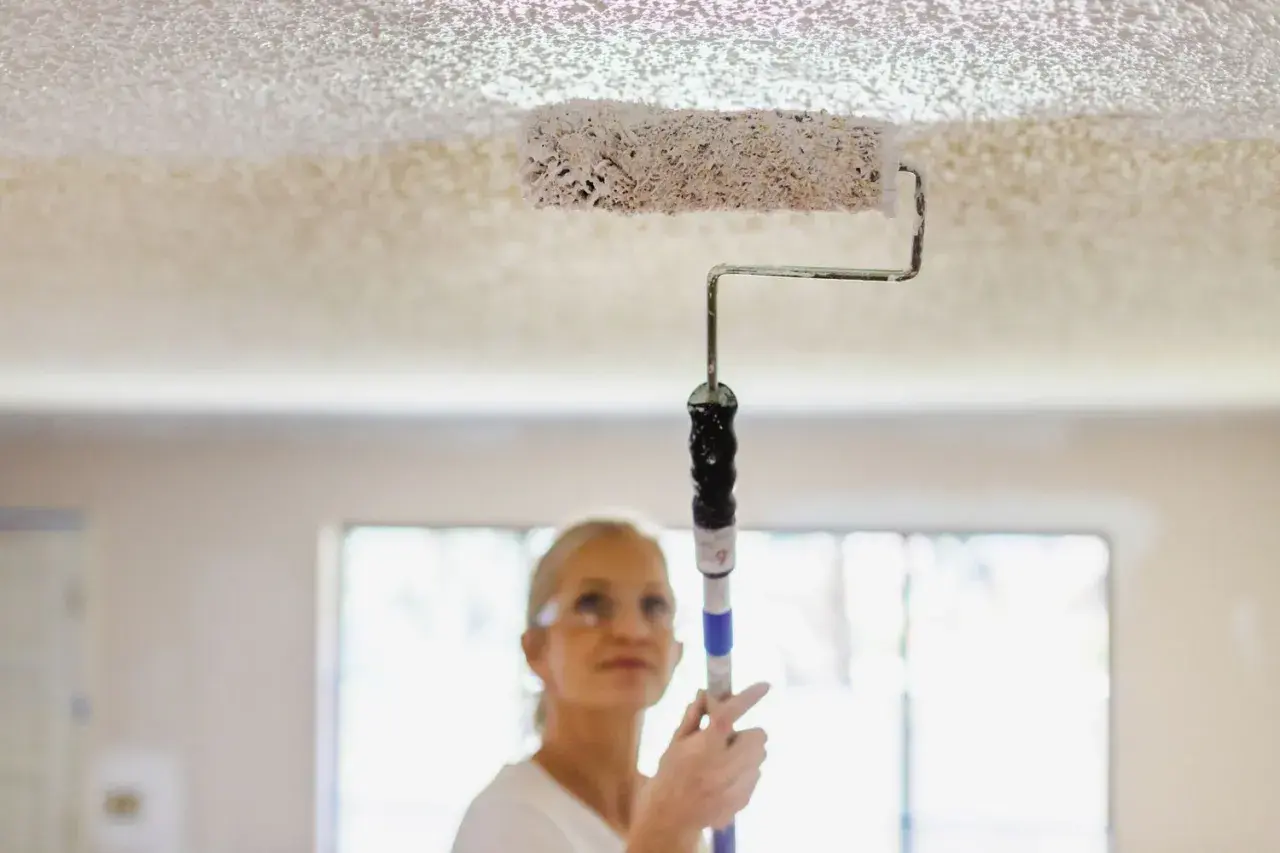 Donna imbianca il soffitto con un rullo, un modo semplice per rinnovare casa.